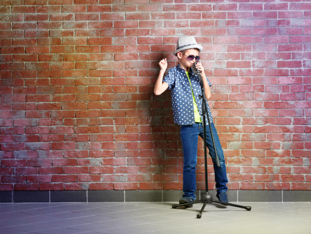 Little boy singing with microphone on a brick wall backgroundの写真素材
