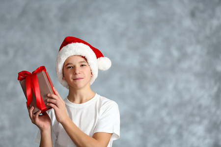 Boy in Santa hat with gift box on grey backgroundの写真素材