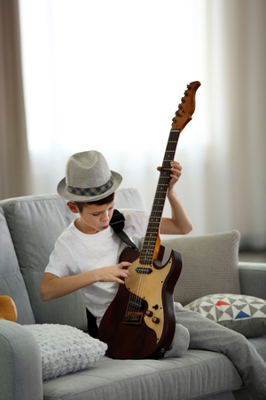 Little boy playing guitar on a sofa at homeの写真素材