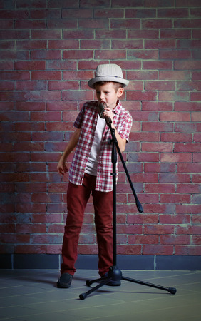 Little boy singing with microphone on a brick wall backgroundの写真素材