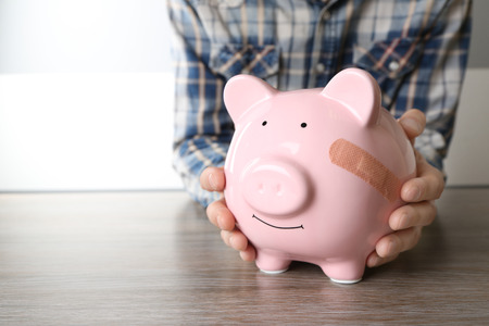 Man holding Piggy Bank with adhesive bandage, on white background