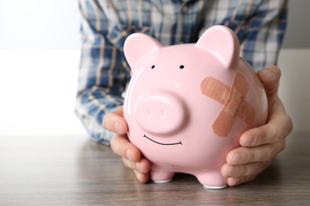 Man holding Piggy Bank with adhesive bandage, on white backgroundの写真素材