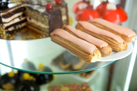 Delicious cakes on glass shelf in confectionery close up