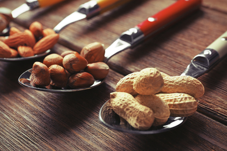 Almonds, hazelnuts and peanuts in the spoons on the wooden table, close-upの写真素材