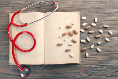 Book, pills and stethoscope on wooden table closeupの写真素材