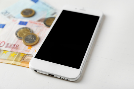 Smart phone and euro banknotes with coins on light table. Telephone chargesの写真素材