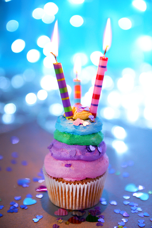 Cupcake with varicolored cream icing and candles on a glitter background, close upの写真素材