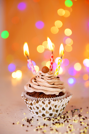Tasty chocolate cupcake with butter cream and candles on a glitter background, close upの写真素材