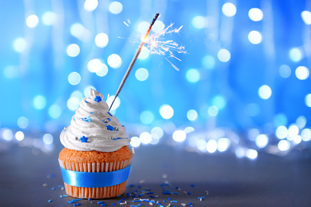 Cupcake with white cream icing and sparkler on a glitter backgroundの写真素材
