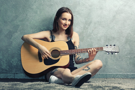 Attractive woman with tattoo playing guitar on grey backgroundの写真素材
