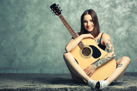 Woman with tattoo and guitar sitting on grey backgroundの写真素材