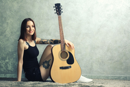 Woman with tattoo and guitar sitting on grey backgroundの写真素材