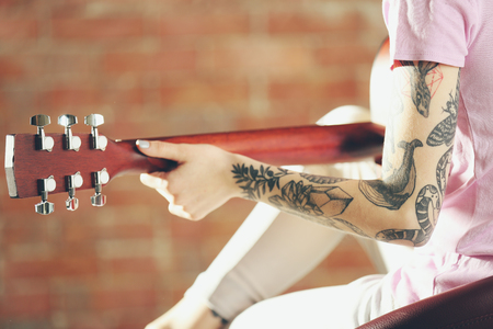 Woman with tattoo playing guitar on brick backgroundの写真素材