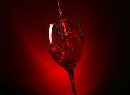 Wine pouring in glass on dark red backgroundの写真素材