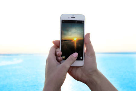 Female hands holding smart phone and taking photo of sunsetの写真素材