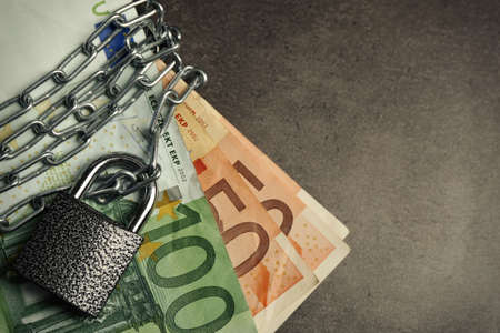 Euro banknotes with lock and chain on gray background