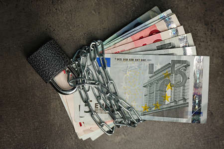 Euro banknotes with lock and chain on gray background