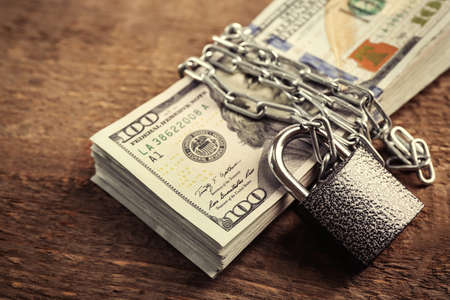 Dollars currency with lock and chain on wooden background