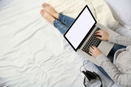 Woman using laptop with headphones on her bed
