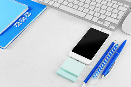 Workplace with mobile phone, keyboard and stationery on light table