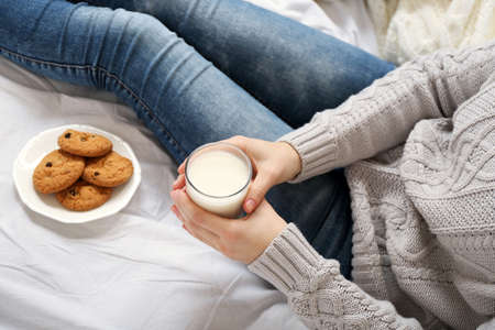 Woman drinking milk with cookies on her bedの写真素材