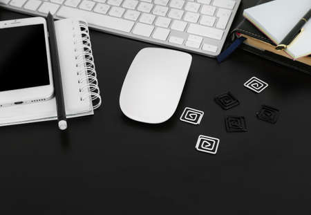 Workplace with mobile phone, computer peripherals and stationery on black table
