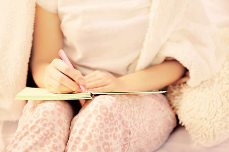 Woman in pajamas writing diary on her bedの写真素材