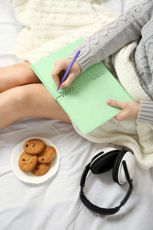 Woman with headphones writing diary on her bed
