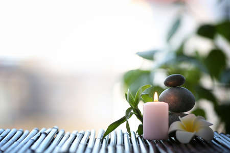 Spa stones with candle and tropical flower on blurred background