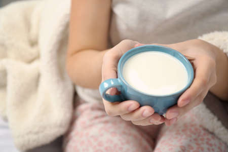 Woman in pajamas holding cup of milk on her bedの写真素材
