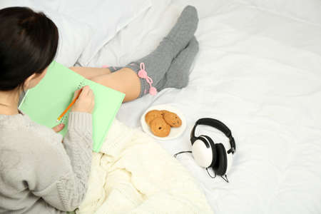 Woman with headphones writing diary on her bedの写真素材