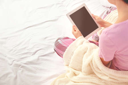 Woman in pajamas using a tablet on her bedの写真素材