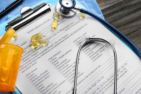 Medical stethoscope, clipboard, pills and coat on the table, close-up