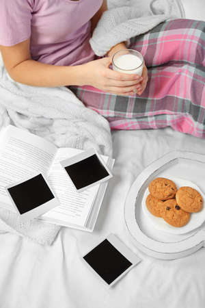 Woman in pajamas looking at photos on her bedの写真素材