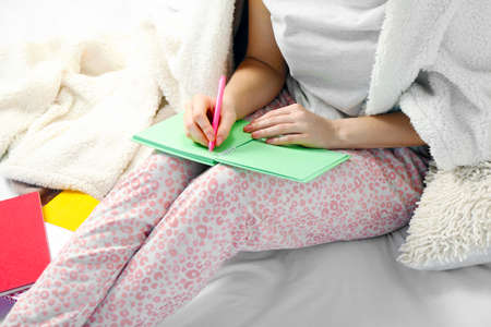 Woman in pajamas writing diary on her bedの写真素材