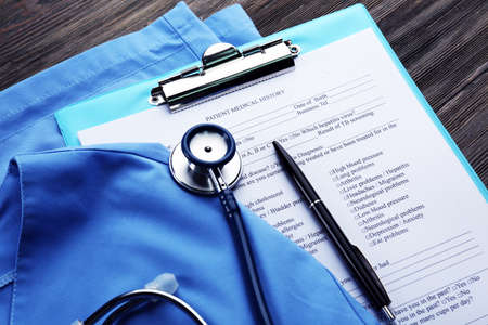 Medical stethoscope, clipboard and coat on the table, close-upの写真素材