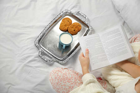 Woman in pajamas reading a book on her bed