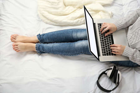 Woman using laptop with headphones on her bedの写真素材
