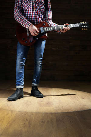 Young man playing electric guitar on lighted dark background