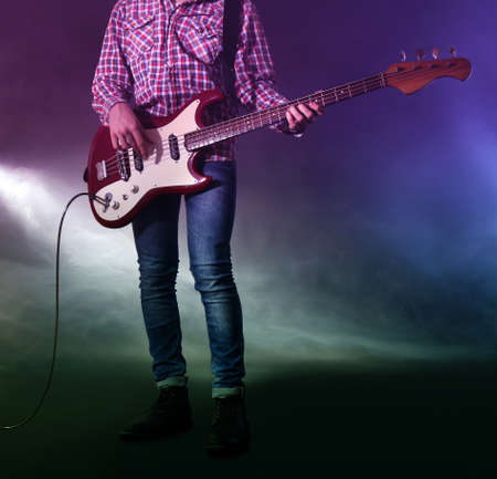 Young man playing electric guitar on lighted foggy background