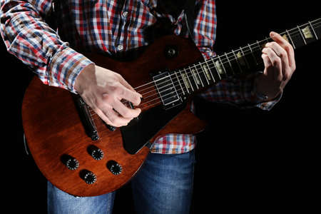 Young man playing electric guitar on lighted dark background