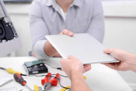 Young man giving broken laptop to repairer in service center