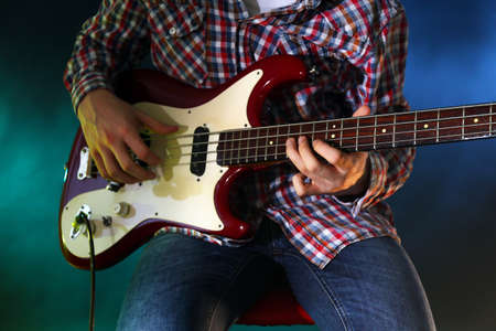 Young man playing electric guitar on lighted dark background