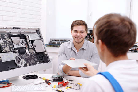 Young man giving broken laptop to repairer in service center
