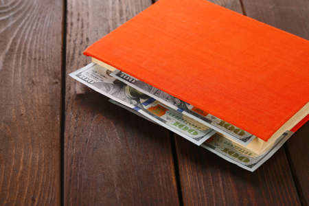 Red book with nested dollar banknotes on wooden table. Stash of money
