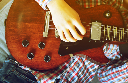 Young man playing electric guitar on grey sofa at homeの写真素材