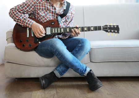 Young man playing electric guitar on grey sofa at homeの写真素材