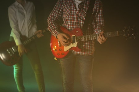 Young couple playing electric guitars on lighted foggy backgroundの写真素材