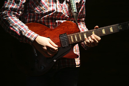 Young man playing electric guitar on dark lighted backgroundの写真素材