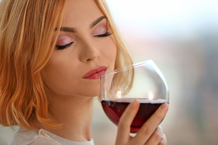 Young woman with glass of red wine on light blurred backgroundの写真素材